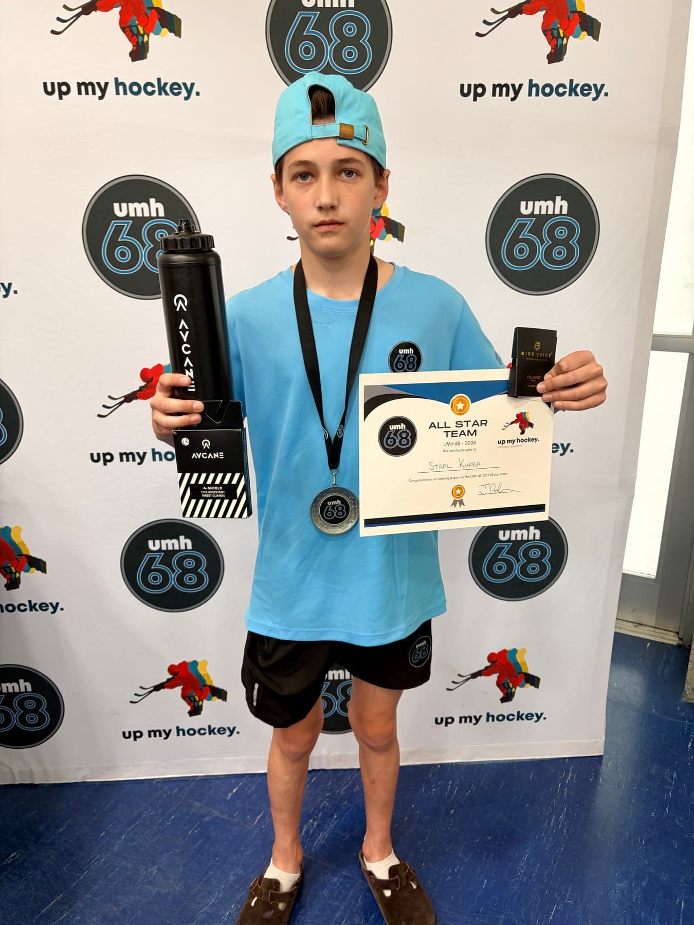 A UMH-68 player wearing a medal and holding an All Star Team certificate in front of the event backdrop.