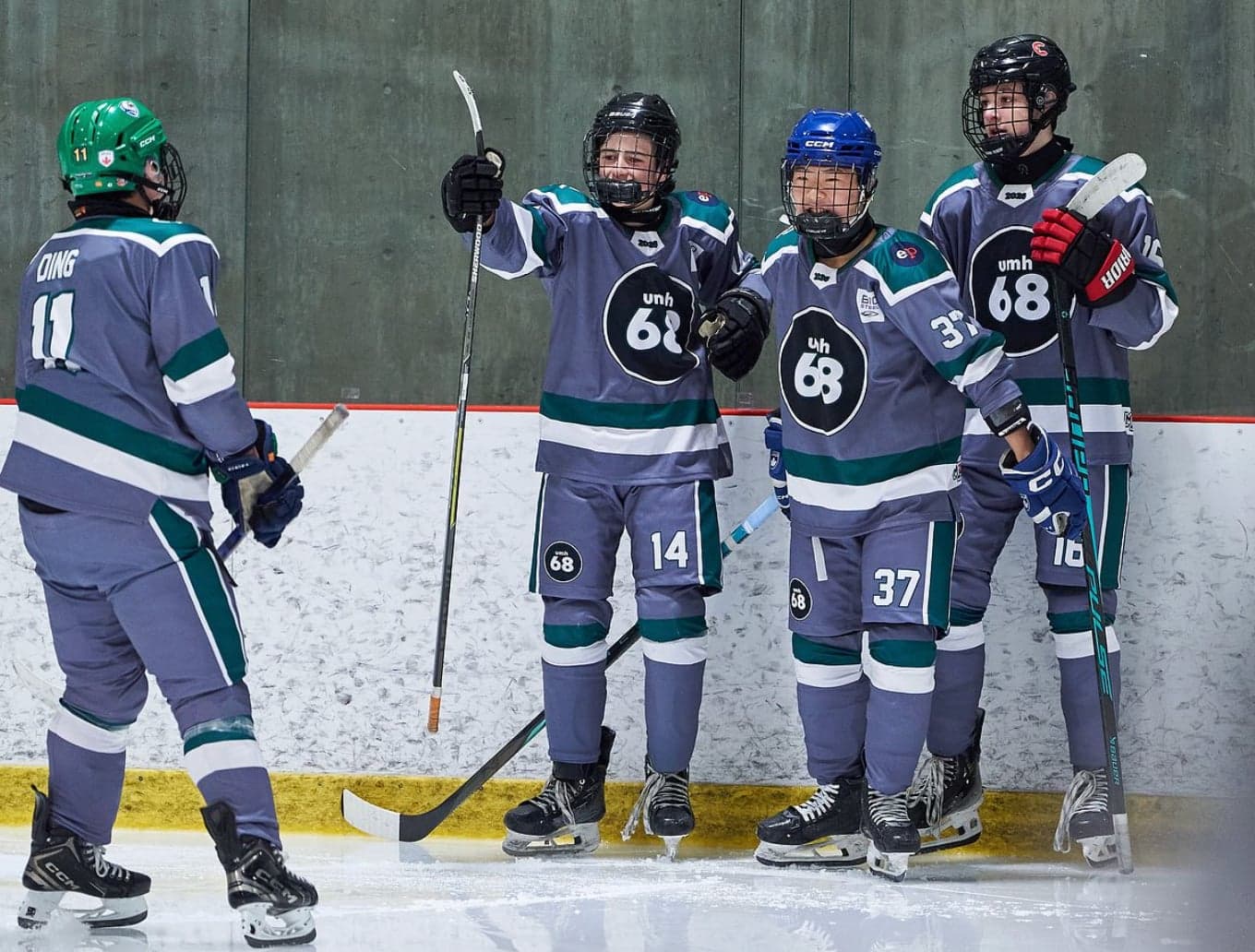 Four UMH-68 teammates in grey and teal jerseys gathered beside the boards on the ice.