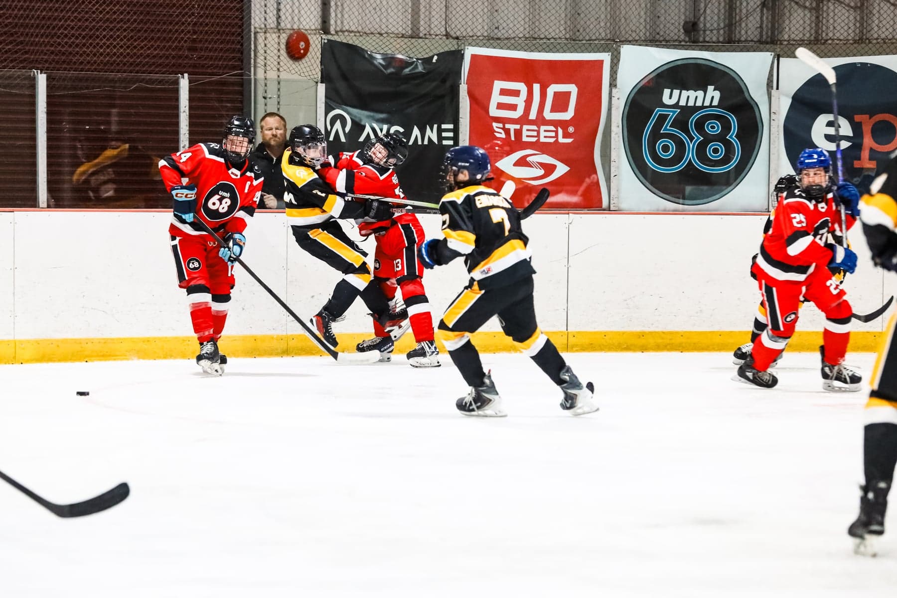 Red and black-and-gold players compete along the boards beneath UMH-68 and sponsor banners.