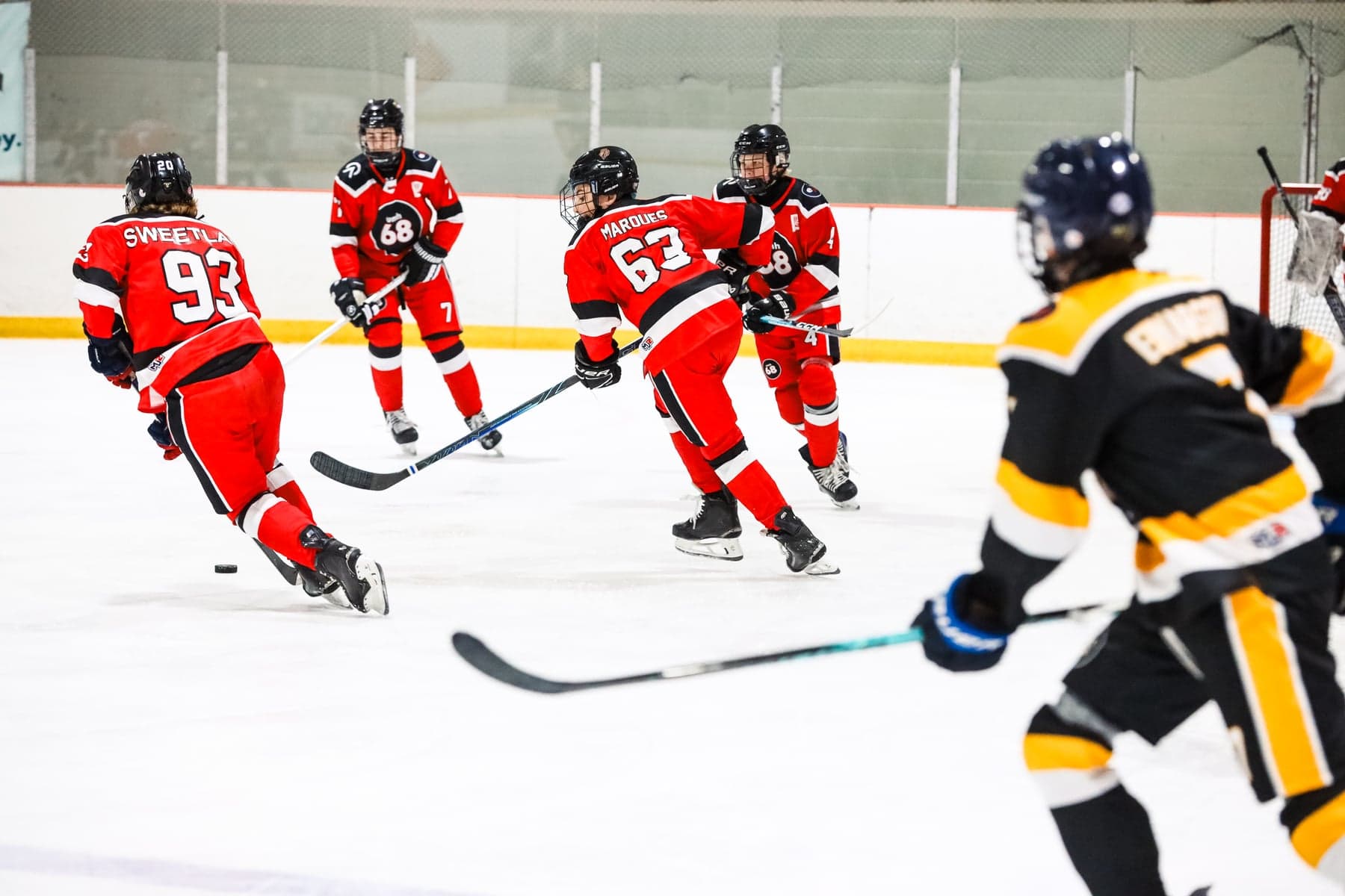Red-jersey teammates follow the puck as a black-and-gold opponent approaches.