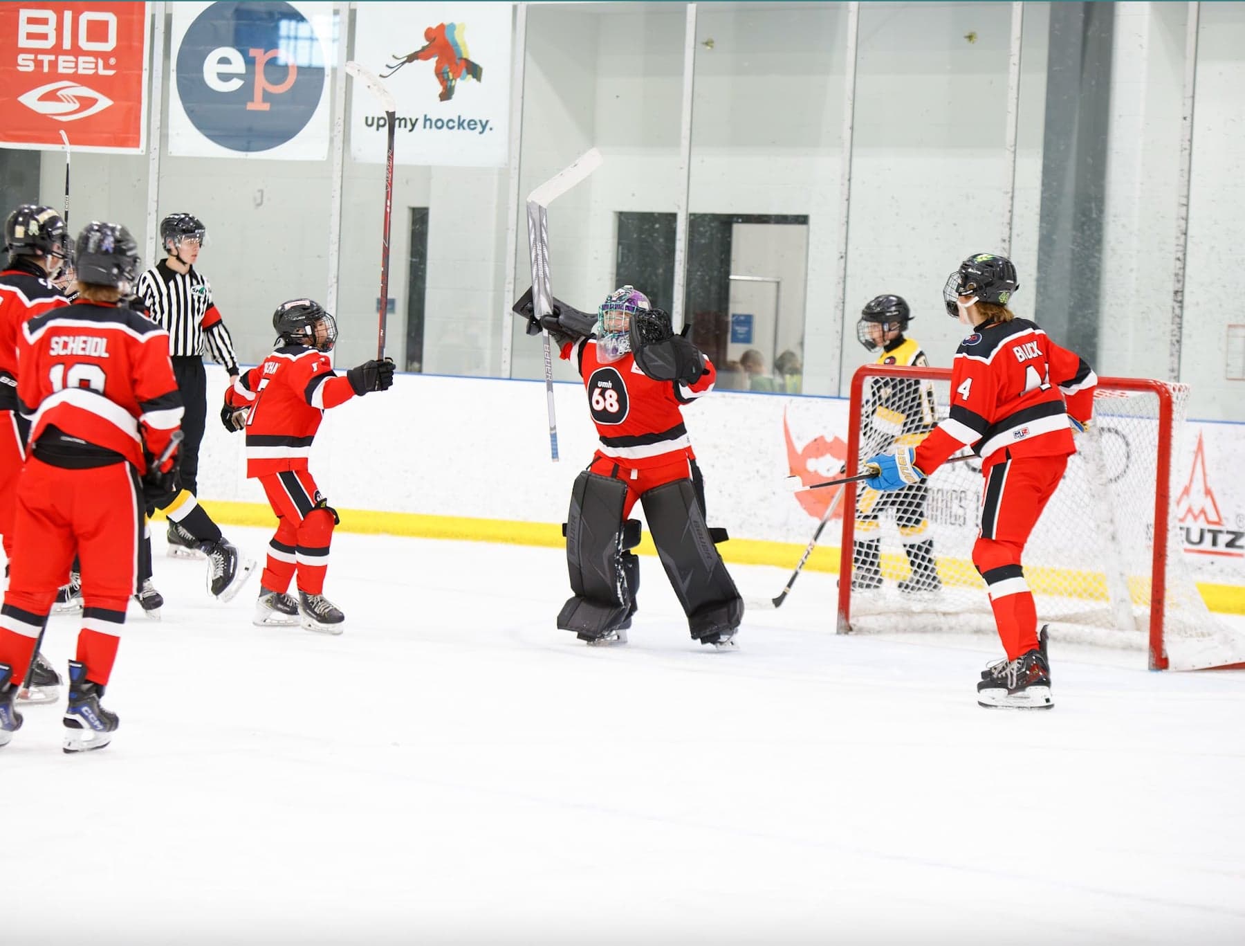 A red-jersey goalie raises both arms as teammates celebrate beside the net.