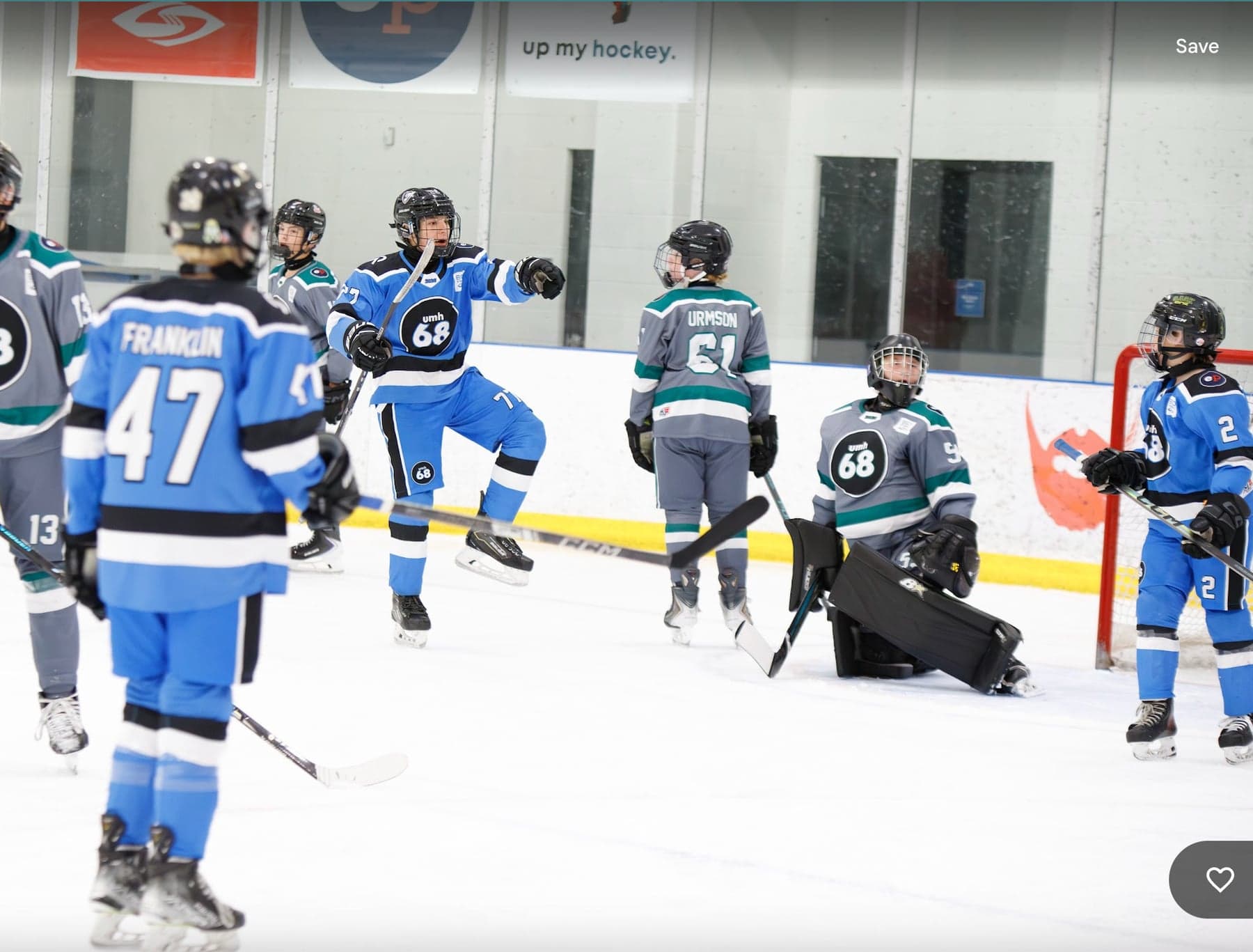 Blue-jersey players celebrate near a grey-and-teal goalie at the net.