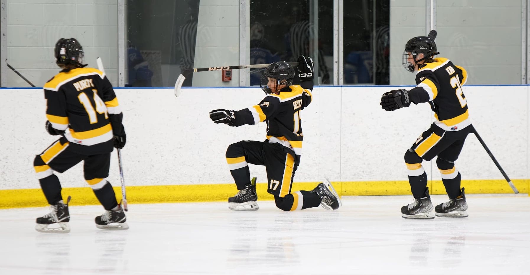 Black-and-gold teammates celebrate as a player drops to one knee with his stick raised.