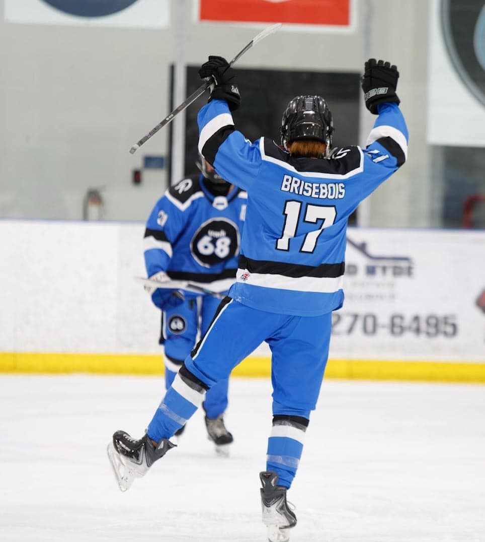 A blue-jersey UMH-68 player raises both arms in celebration on the ice.