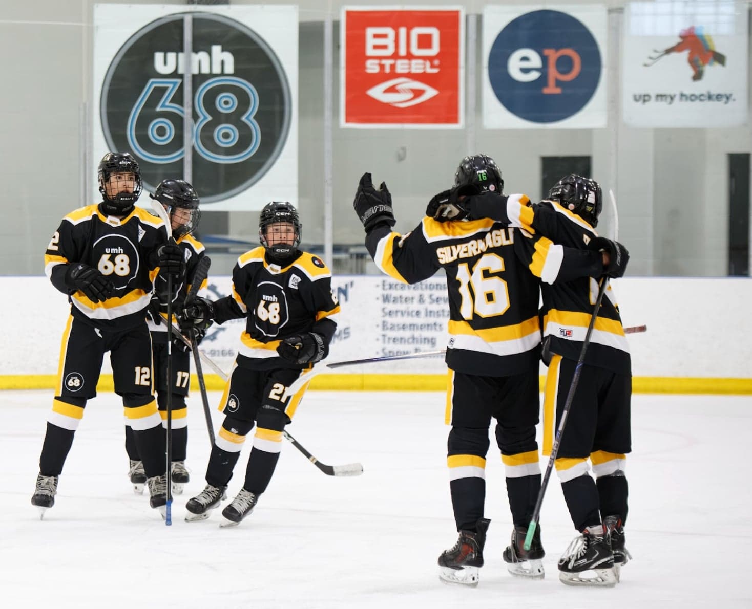 Black-and-gold teammates celebrate beneath UMH-68 and sponsor banners.