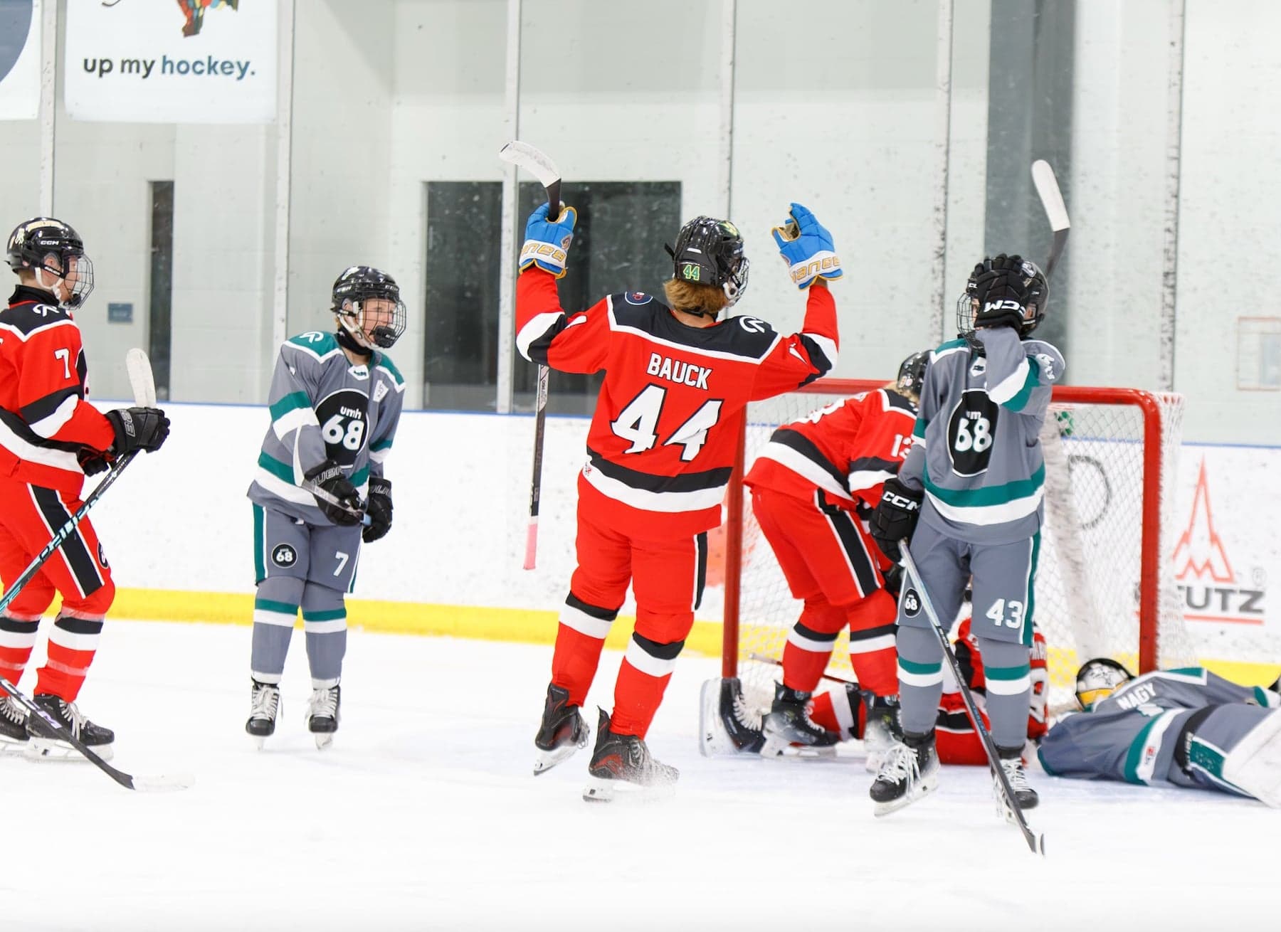 A red-jersey player raises his arms beside the net among grey-and-teal opponents.