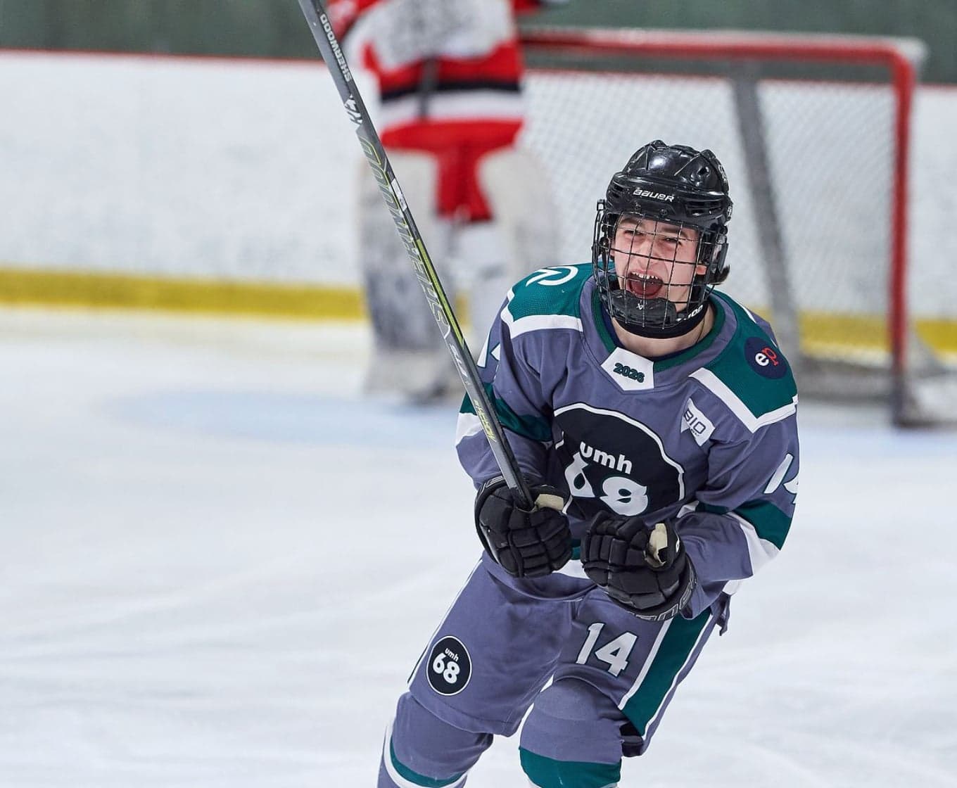 A grey-and-teal UMH-68 player celebrates with his hockey stick raised