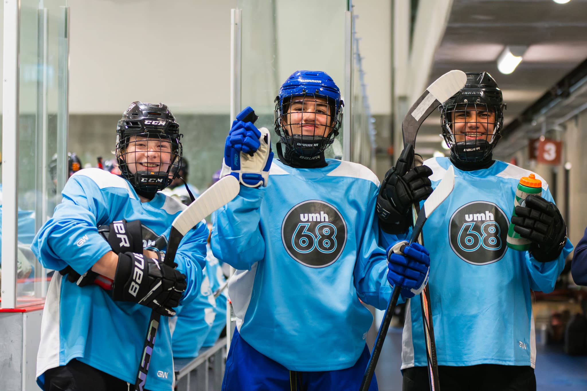 Three UMH-68 players in blue jerseys smiling together at the rink